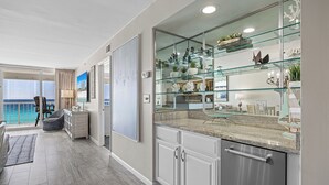 A modern kitchen with a glass display cabinet, a dining area with a view of the ocean, and a balcony with a chair. - Reel Paradise - Destin Gulfgate 0505! (Destin)