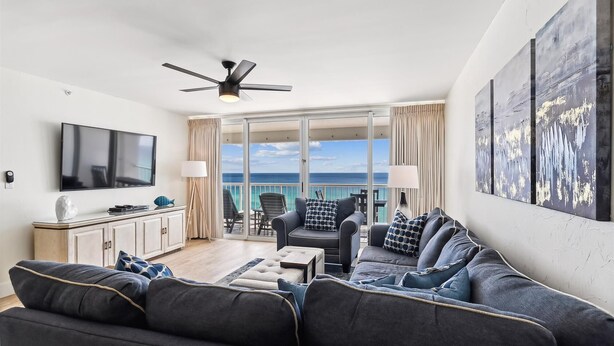 A modern living room with a flat-screen TV, a ceiling fan, and a large window overlooking the ocean. - Where every hour is Happy Hour - Destin Gulfgate 0602! (Destin)