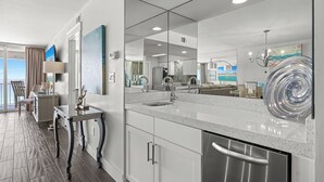 A modern kitchen with a large island, a dining area with a table and chairs, and a view of the ocean through a large window. - Good Times and Tan Lines - Destin Gulfgate 0603! (Destin)
