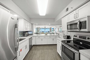 Une cuisine moderne dotée d’appareils électroménagers en acier inoxydable, de meubles blancs et offrant une vue sur l’extérieur.