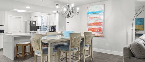 A modern kitchen with a central island, a dining area with a glass table and chairs, and a living area with a couch.