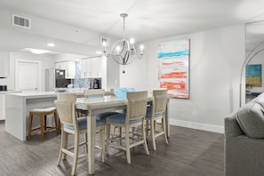 Una cocina moderna con una isla central, un comedor con mesa y sillas de vidrio, y una sala de estar con un sofá.