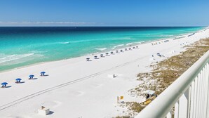 Una playa con arena blanca, agua turquesa cristalina y sombrillas azules.