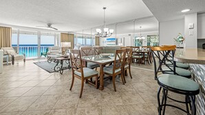 Amplia sala de estar con balcón, comedor con sillas de madera y mesa de vidrio, y cocina con electrodomésticos modernos.