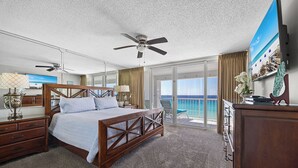 Habitación de hotel con cama, ventilador de techo, televisión y balcón con vista al océano.