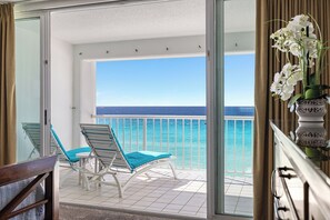 A balcony with a view of the ocean, a chair, and a vase with flowers.
