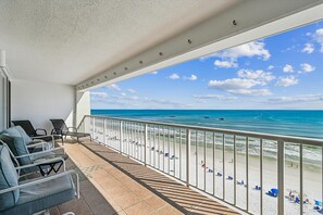Varanda com vista para a praia, equipada com cadeiras e guarda-corpo.