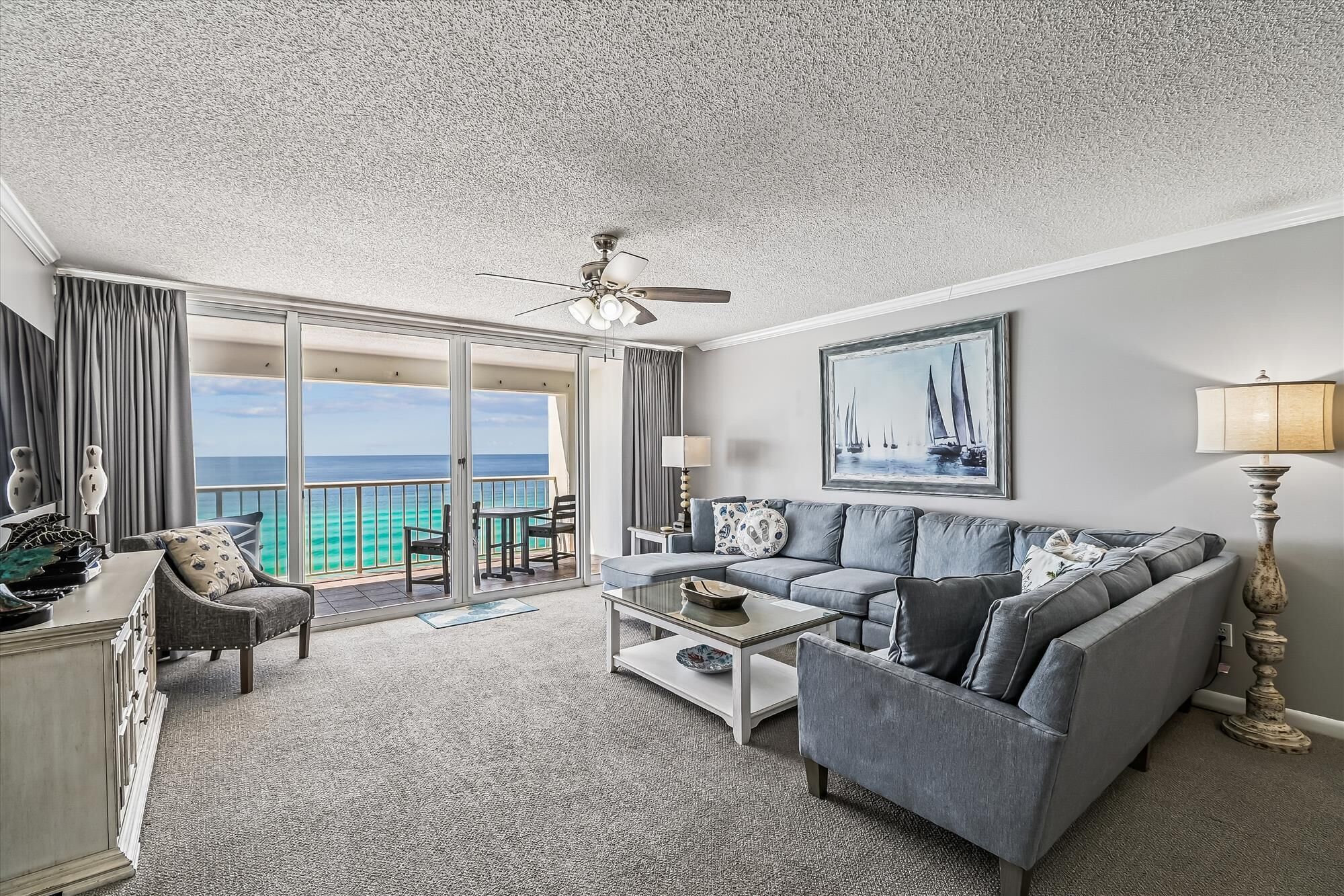 A spacious living room with a gray sofa, a coffee table, and a view of the ocean through large sliding glass doors.