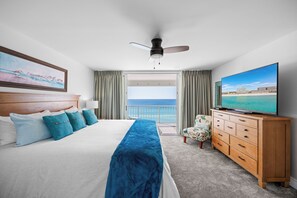 Ein Hotelzimmer mit Bett, Fernseher, einem Holzschrank und einem Balkon mit Meerblick.