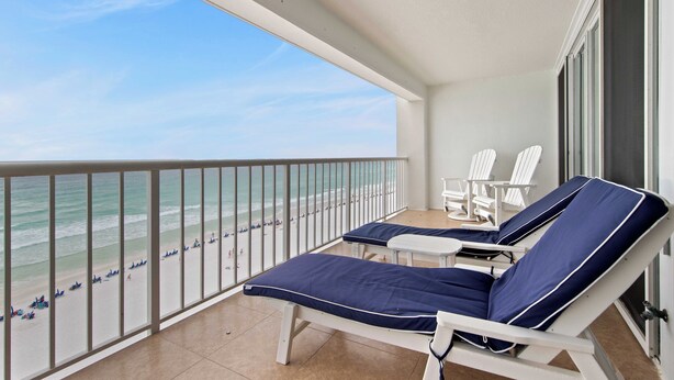 Ein Balkon mit zwei Loungestühlen, einem kleinen Tisch und Blick auf den Strand.