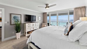 Ein Schlafzimmer mit einem großen Bett, einem Deckenventilator, einem Fernseher, einer Topfpflanze und Meerblick durch große Fenster.