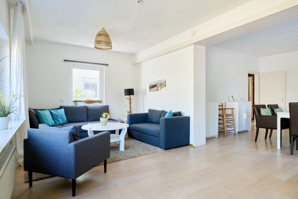 A modern living room with a sofa set, a dining area, and a kitchen in the background.