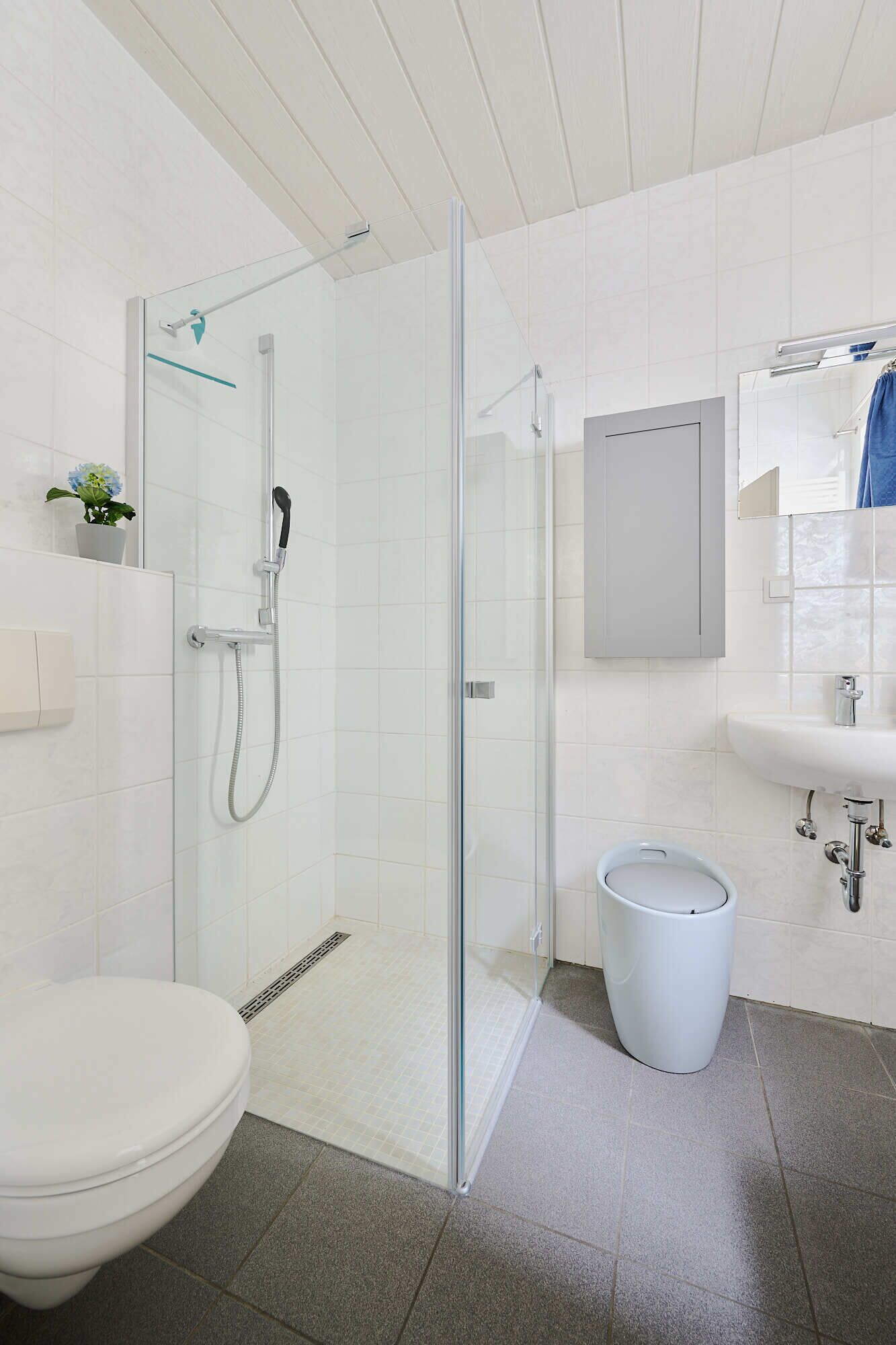 Un baño moderno con ducha de vidrio, inodoro blanco, lavamanos y un pequeño cubo de basura.