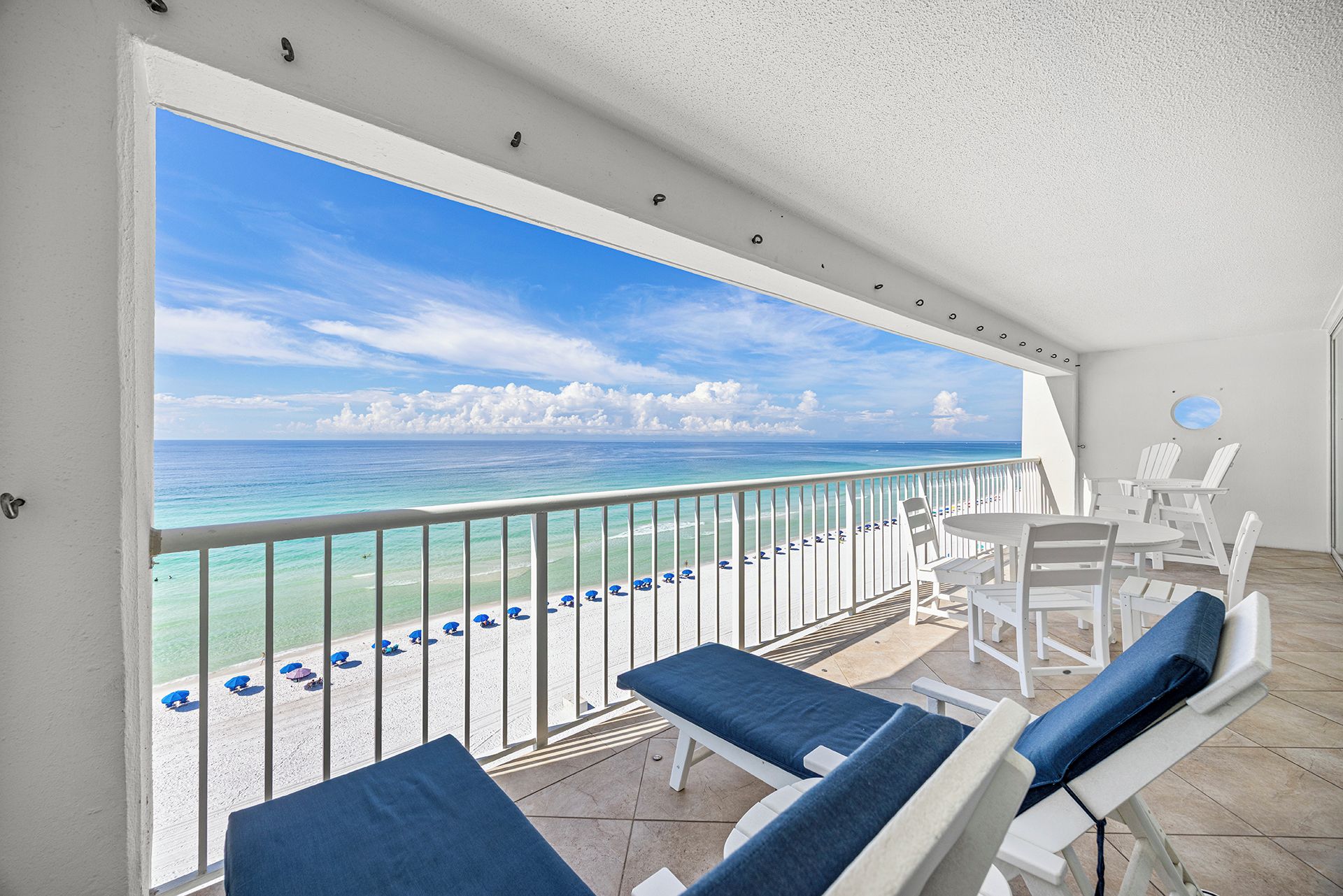 A balcony with a view of the ocean, white chairs, and a table.