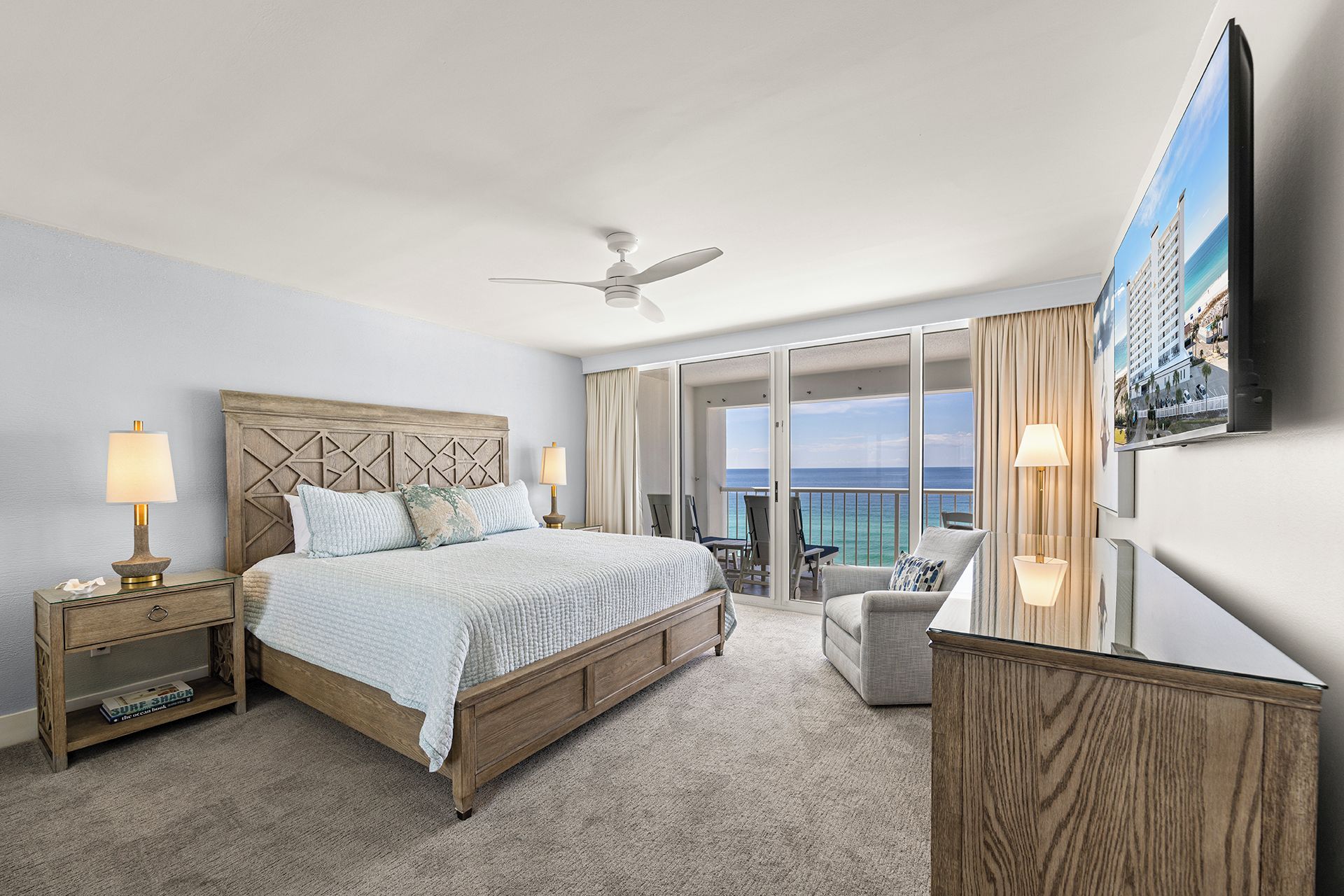 Quarto de hotel com cama, ventilador de teto, varanda com vista e televisão na parede.