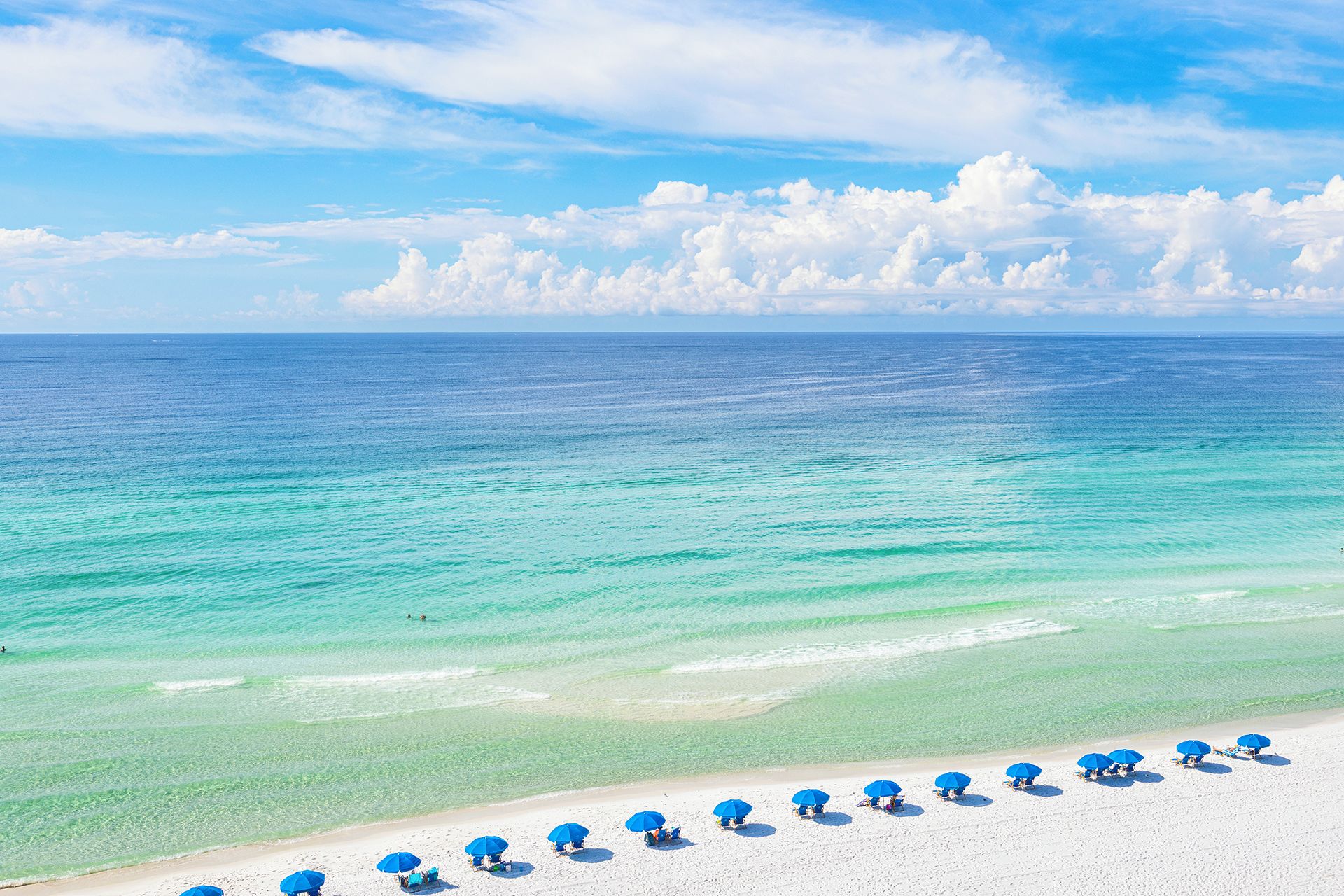 A beach with clear turquoise water and a row of blue umbrellas.