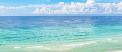 A beach with clear turquoise water and a row of blue umbrellas.