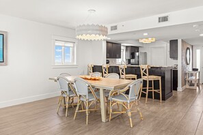 A modern kitchen with dark cabinetry, a wooden dining table, wicker chairs, and pendant lighting.