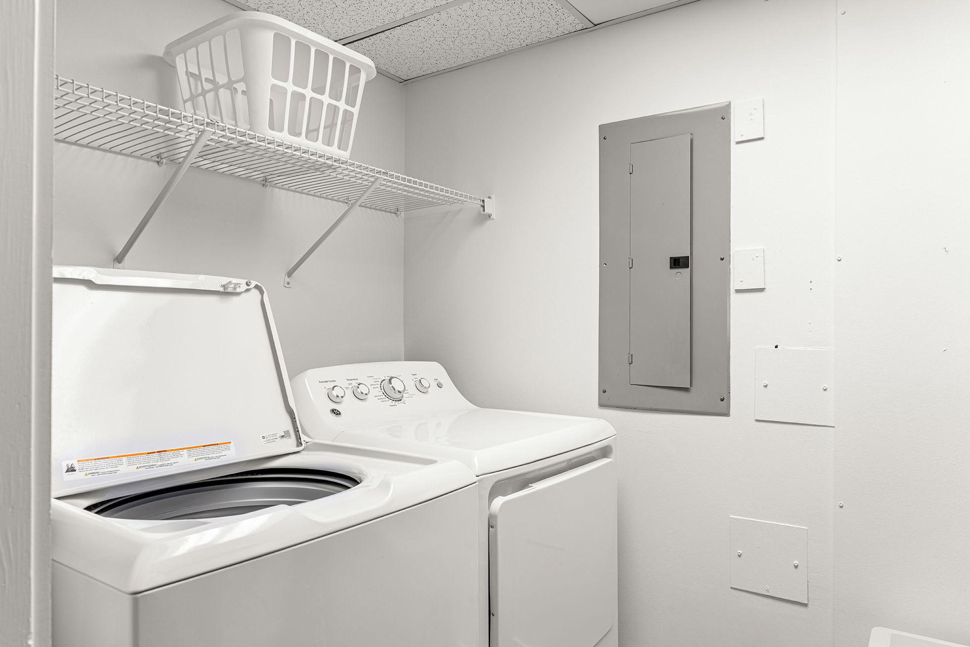 A laundry room with a front-loading washing machine, a drying rack, and a utility room door.