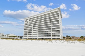 Ein Hochhaus-Hotel mit mehreren Balkonen, direkt an einem Sandstrand unter blauem Himmel gelegen.