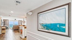 Un vaste espace de vie agrémenté d’un grand tableau représentant un paysage côtier, un coin repas et une vue sur l’océan grâce à de grandes fenêtres.