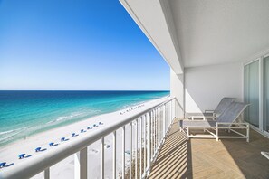 A balcony with a view of a beach, white railing, and two lounge chairs.