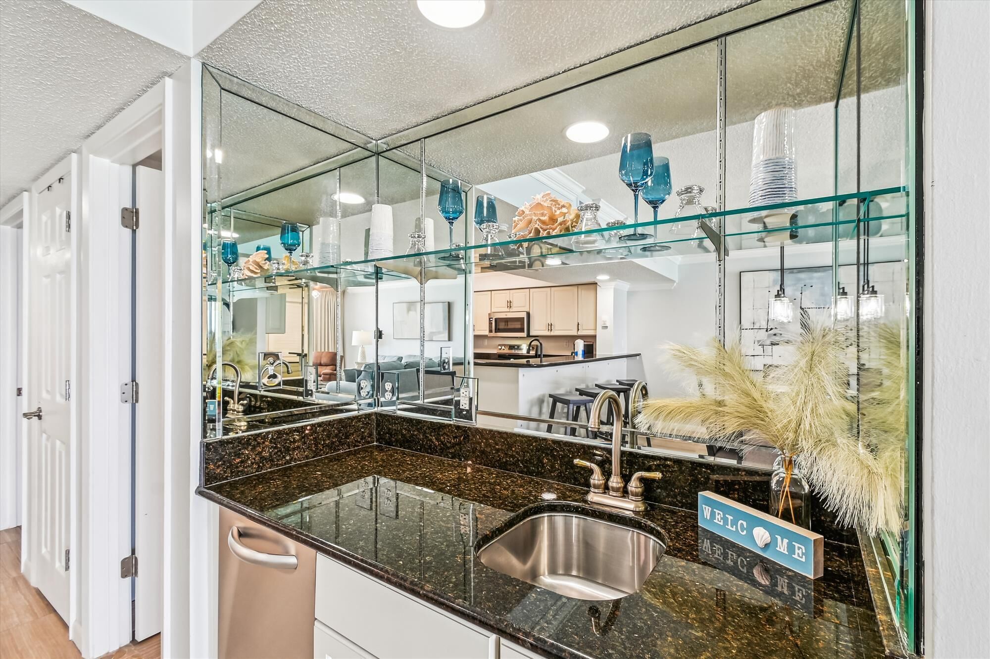 A modern kitchen with a large glass backsplash, stainless steel sink, and a welcome sign.