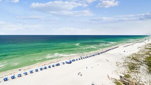 A beach with rows of blue umbrellas and a wooden boardwalk leading to the water. - All Decked Out - Destin Gulfgate 0904! (Destin)