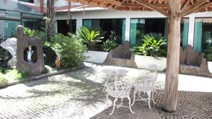 Un patio al aire libre con una pérgola de madera, sillas de metal blanco y una mesita redonda.