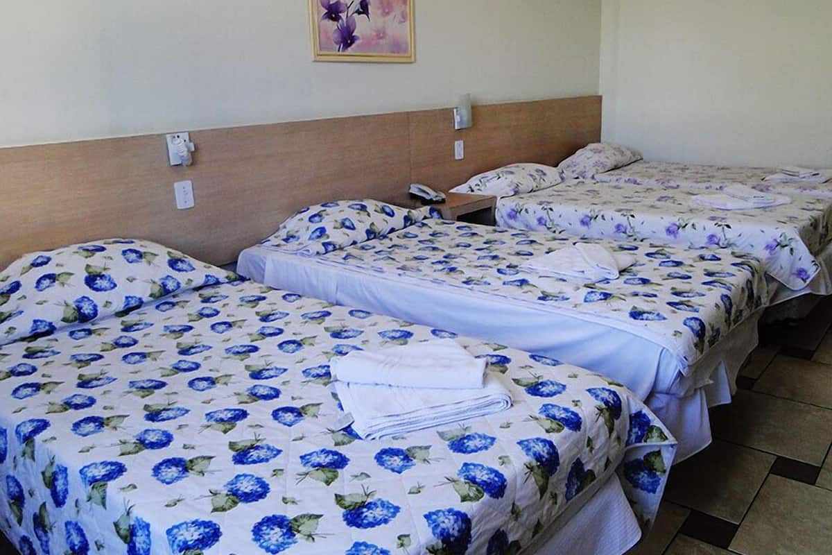 Habitación de hotel con tres camas, cada una con ropa de cama floral. Un cuadro cuelga de la pared sobre las camas.