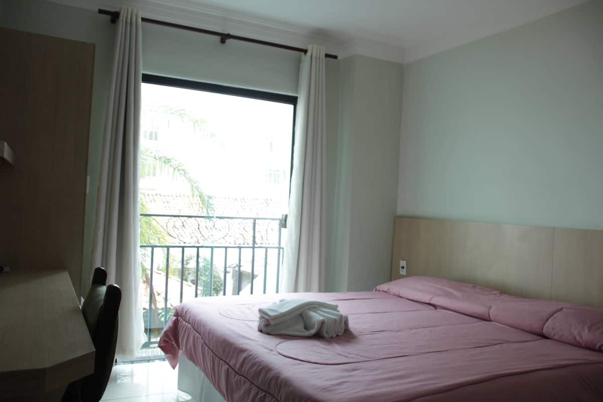 Una habitación de hotel con una cama, un escritorio y un ventanal con cortinas.