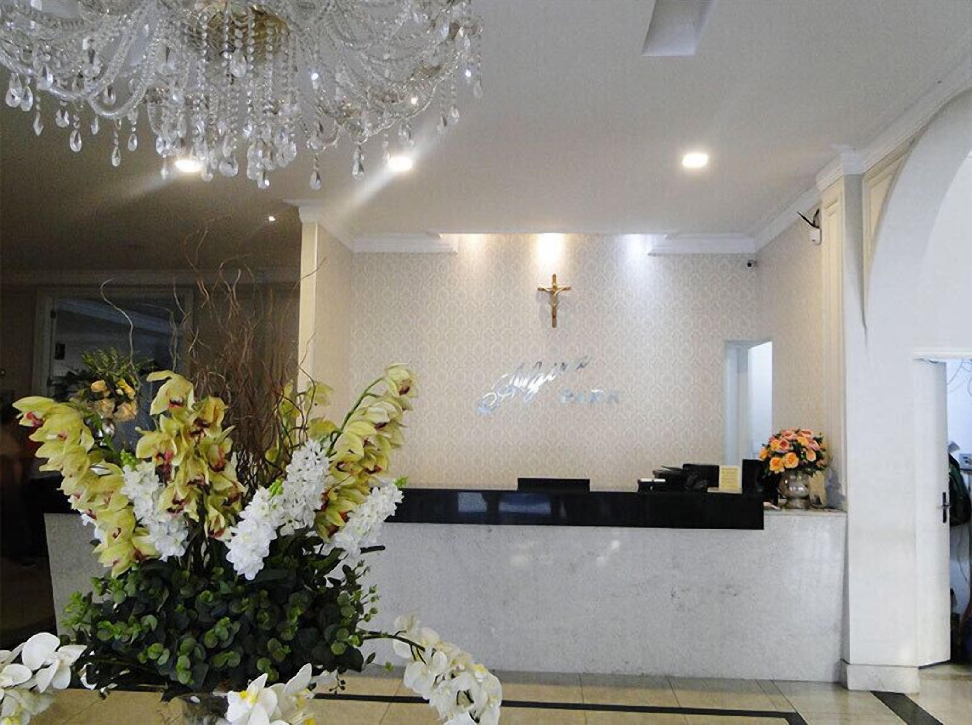 Uma área de recepção com uma cruz na parede, um candelabro e um arranjo floral.