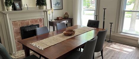 Un comedor con una mesa de madera, sillas grises tapizadas, una chimenea y vistas al exterior a través de amplias ventanas.