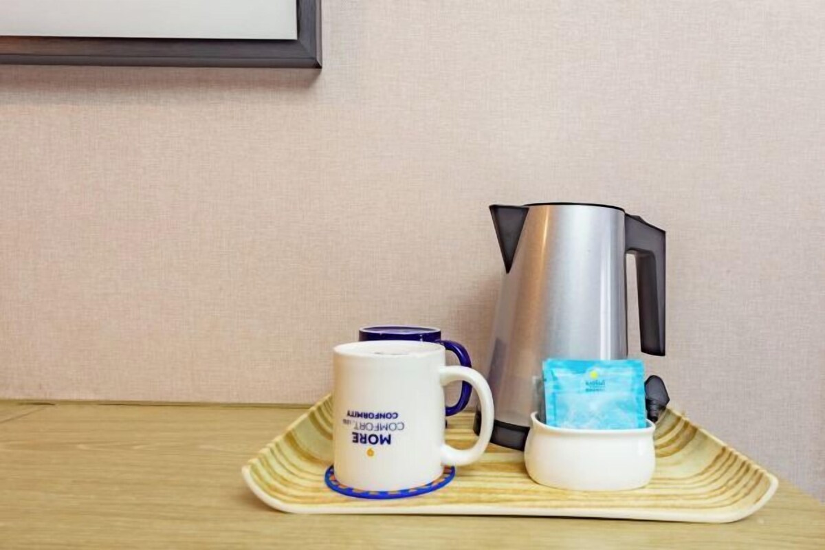 A tray with a coffee maker, a mug, and a packet of tea on a wooden table.