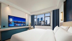 Quarto de hotel com uma cama grande, televisão de tela plana na parede, janela com vista para a cidade e escrivaninha com cadeira.