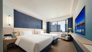 Quarto de hotel com duas camas, uma escrivaninha, uma cadeira, uma televisão e vista para a paisagem urbana.