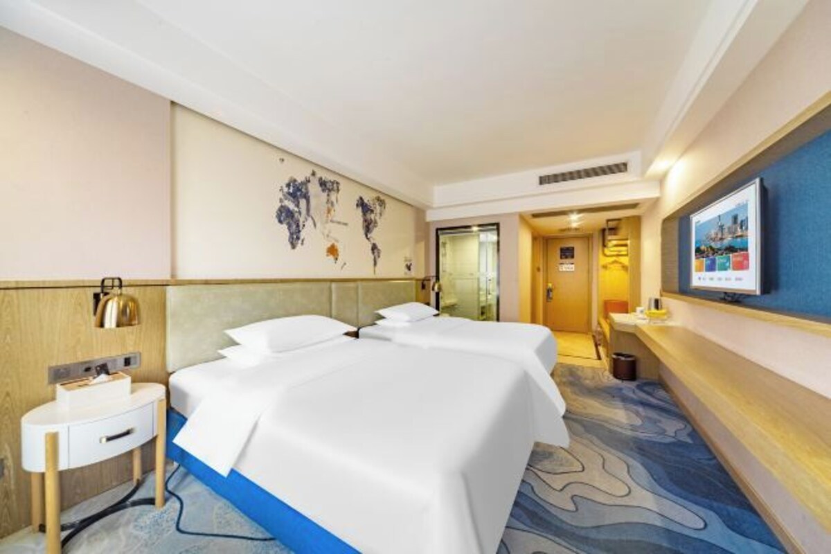 A hotel room with two beds, a small desk, a world map on the wall, and a television on the wall.