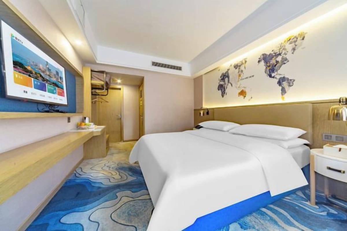 Une chambre d’hôtel avec un grand lit, un téléviseur à écran plat, une carte du monde accrochée au mur et une moquette à motifs.