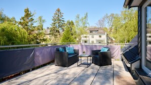 Ein Balkon mit Korbmöbeln, einem kleinen Tisch und Blick auf ein Gebäude und Bäume.