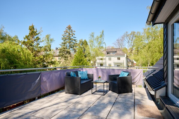 A balcony with wicker furniture, a small table, and a view of a building and trees.