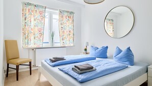 Ein Schlafzimmer mit zwei Betten, einem Sessel, einem Nachttisch mit Lampe und einem Spiegel an der Wand.