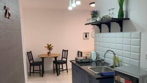 Cocina compacta con armarios oscuros, un lavamanos y un microondas. Hay un comedor con dos sillas y una mesa pequeña.