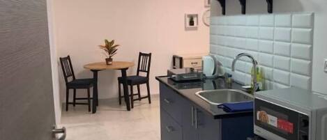 A compact kitchen with dark cabinets, a sink, and a microwave. There is a dining area with two chairs and a small table.