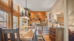 A spacious dining area with a wooden table and chairs, a kitchen in the background, and a staircase leading to another level. - Spacious, Luxury 2BR+Loft Cabin with Fireplace & Balcony - Close to Entertainment! (Branson)