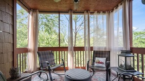 A covered outdoor seating area with wicker furniture, a small table, and a lantern. - Spacious, Luxury 2BR+Loft Cabin with Fireplace & Balcony - Close to Entertainment! (Branson)