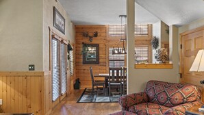 A cozy cabin interior with wooden walls, a dining area, and a patterned sofa. - Spacious, Luxury 2BR+Loft Cabin with Fireplace & Balcony - Close to Entertainment! (Branson)