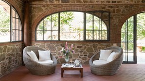 Ein Zimmer mit Steinwänden, zwei Korbstühlen, einem kleinen Tisch mit Blumenvase und großen Bogenfenstern.