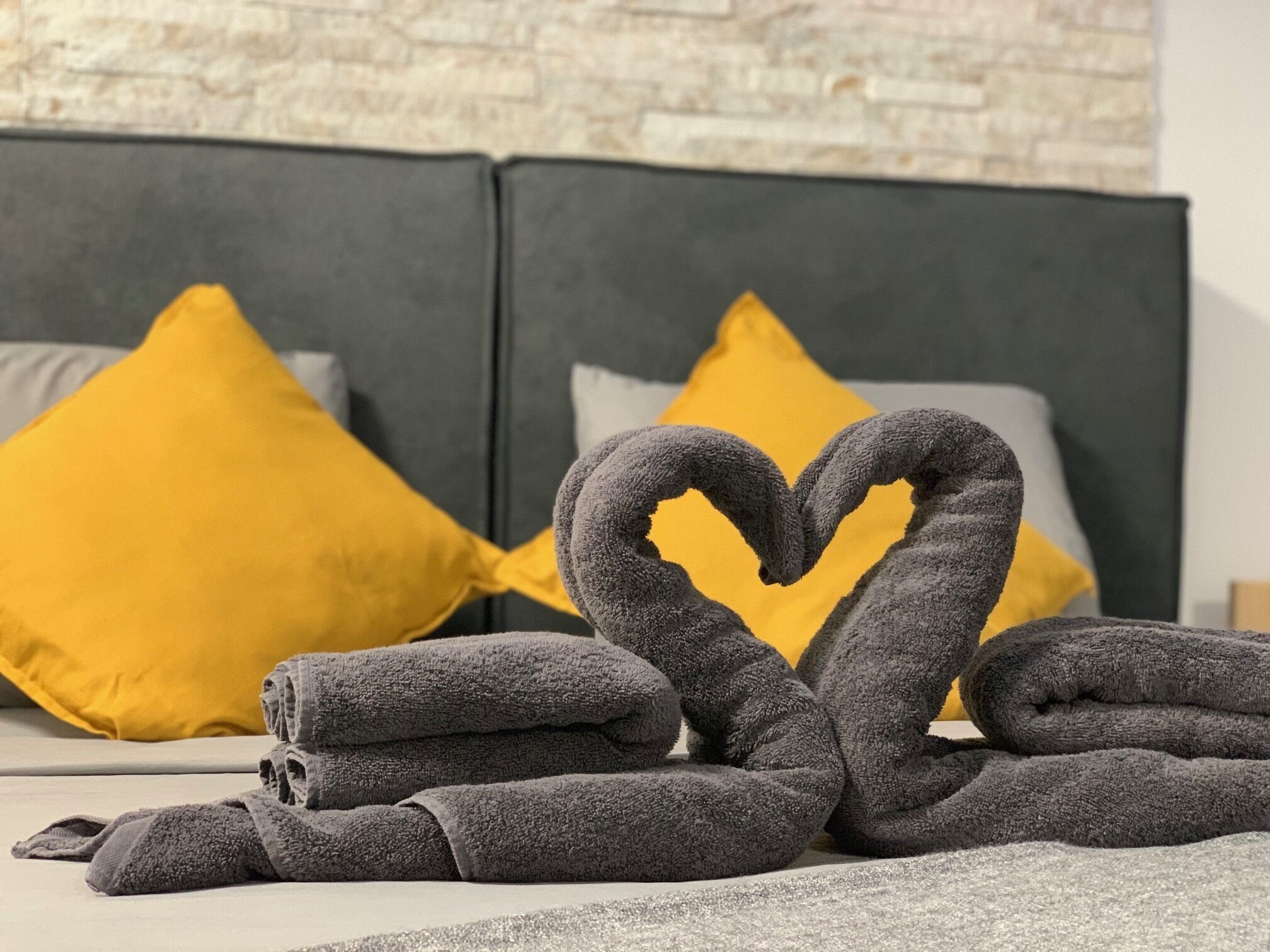 A bed with a heart-shaped towel arrangement, a grey headboard, and two yellow pillows.