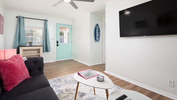 A living room with a black sofa, a white coffee table, a teal door, and a flat-screen TV mounted on the wall. - Serene & Quiet Cottage | Office | 5 Min to RH (Rock Hill)