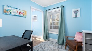 A room with a blue wall, a window with curtains, a painting of birds, a desk, and a chair. - Serene & Quiet Cottage | Office | 5 Min to RH (Rock Hill)